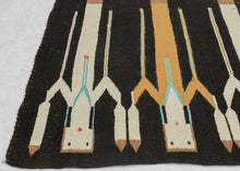 This Yei rug was woven by Navajo weavers during the second quarter of the 20th century in the Southwest United States.  The design of this rug is derived from Navajo sand painting. It features six “Yei” or holy people on a black background. The Yei alternate between orange and white and each is wearing turqoise necklaces and holds sacred eagle feathers.