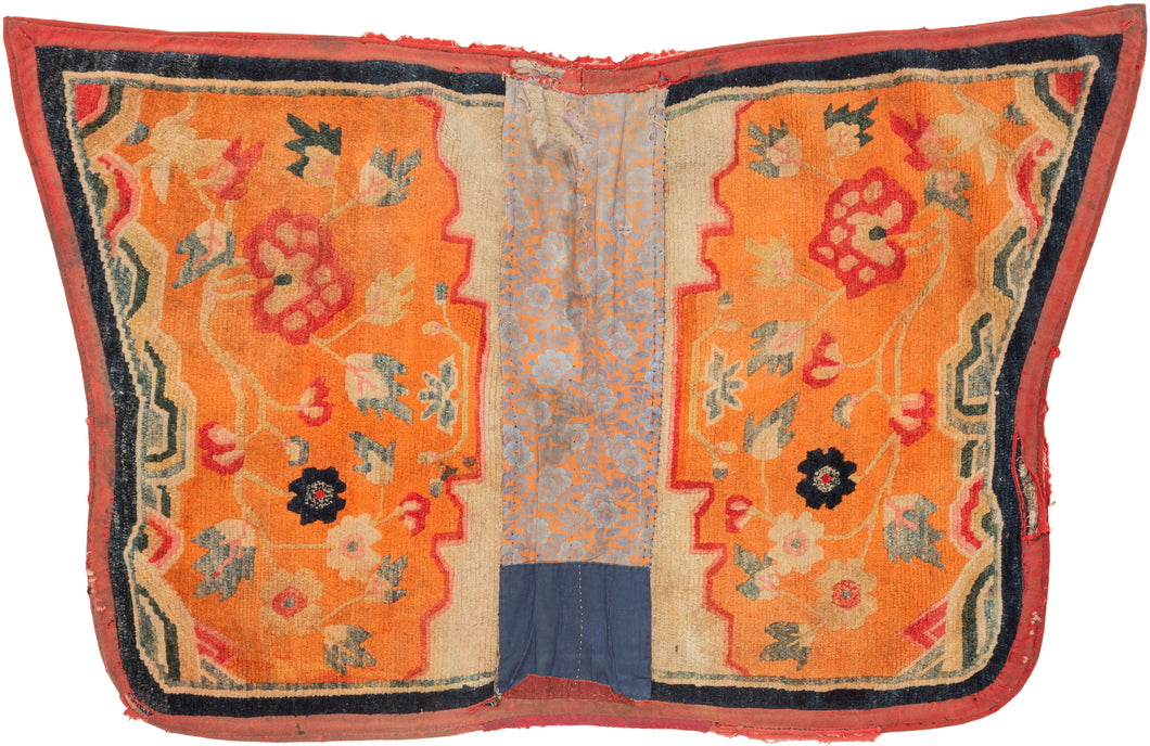 This saddle blanket was woven in Tibet at the turn of the 20th century.  This rugs are known as a Makden and were intended to be used under a horse saddle in Tibet. This piece has been rendered in a beautiful butterfly format. It features two mirror image halves with floral forms growing out of stylized rocks on a vibrant orange ground.