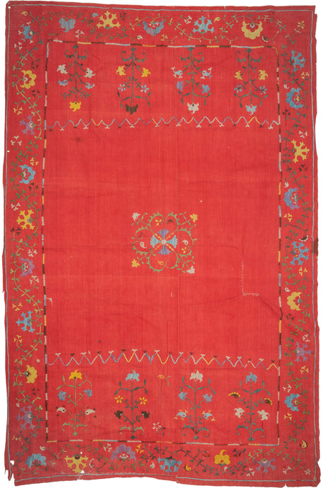 This Suzani was handmade during the early 20th century in Uzbekistan.

This suzani is composed of central floral motif embroidered in silk on an open red cotton field. Flanked by vibrant multi-tiered blossoming flowers to the right and left and framed by a lively floral meander. A multitude of colors are used for the embroidery, including turqoise, green, white, yellow, and purple.