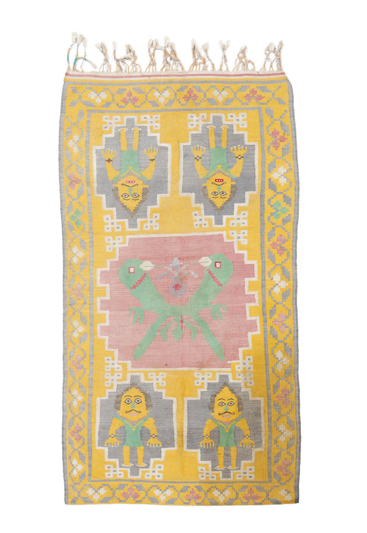 This pictorial dhurrie was handwoven in India during the early 20th century.

It features a central cartouche of two green birds that is surrounded by four moustachied men. The men wear tight green onesies and bracelets on each wrist. In a fun and vibrant palette of bright yellow, pink, green, purple and white.