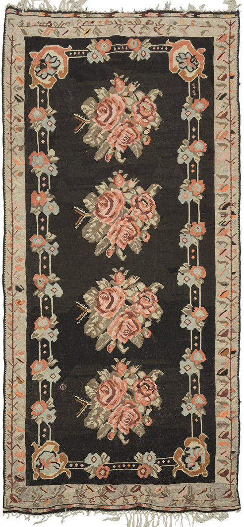 This Bessarabian kilim features four bouquets plush cabbage roses in maroon, orange and soft pink on a deep brown, almost black field. It has a small inner frame of pairs of simpler flowers on a track with c scroll cornices. The proper outer border features a scrolling view with various leaves in bright oranges, slate and soft pinks on a camel ground. 