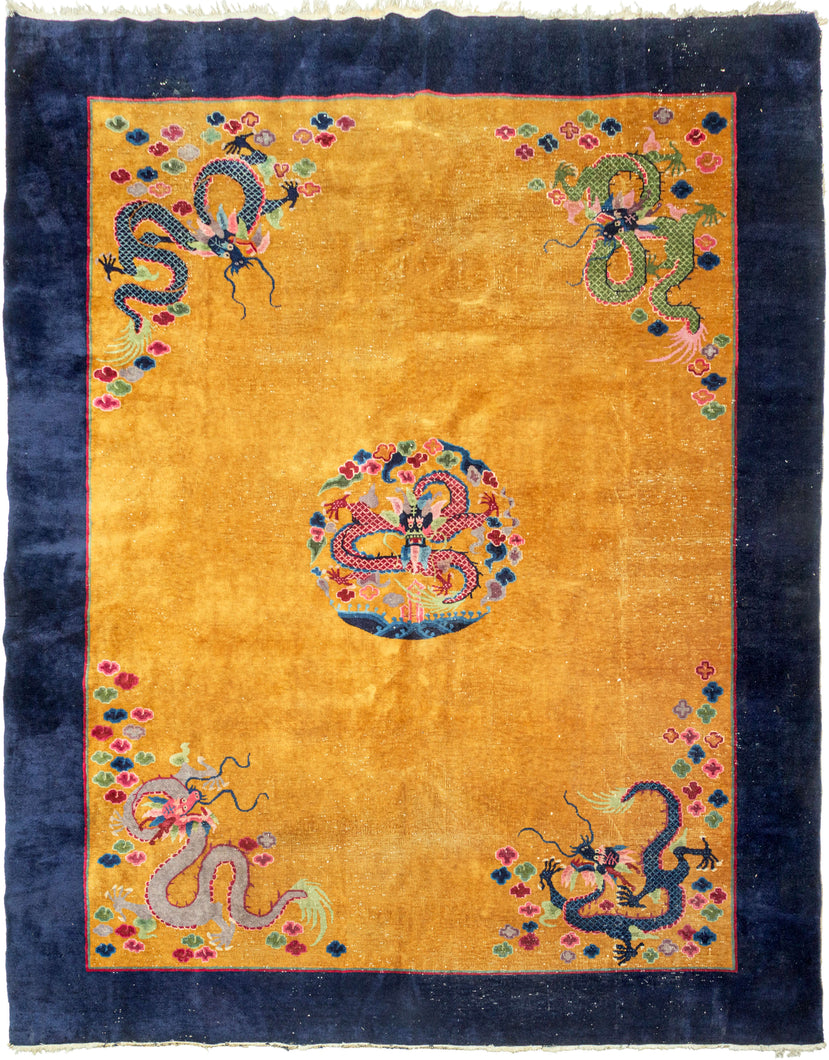 This Art Deco rug was handwoven in Tientsin, China during the second quarter of the 20th century. 

This Deco rug features a central dragon surrounded by additional dragons in each of it's four corners all atop an open golden yellow ground framed by a thick unadorned navy border. The scaly and serpentine dragons come in a variety of tones and are each surrounded by colorful cloudbands which emphasize that they are in flight. In China the dragon is often depicted winglessly flying through clouds. I