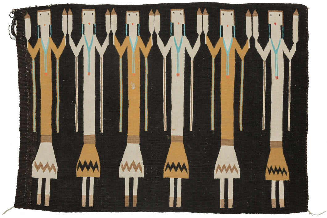 This Yei rug was woven by Navajo weavers during the second quarter of the 20th century in the Southwest United States.  The design of this rug is derived from Navajo sand painting. It features six “Yei” or holy people on a black background. The Yei alternate between orange and white and each is wearing turqoise necklaces and holds sacred eagle feathers.