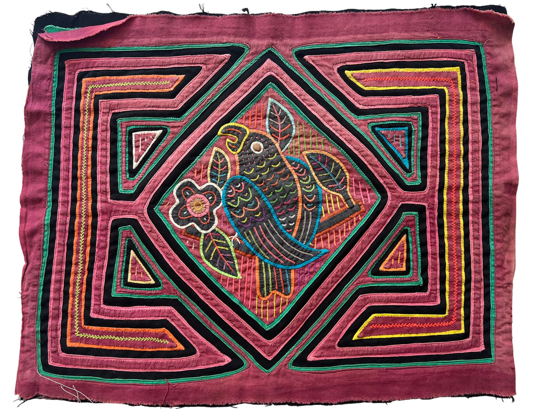 Vintage Mola cloth handmade by the Guna (previously spelled Kuna) people of the San Blas Islands.  Mola is a reverse appliqué technique, similar to the technique used in quilting but using multiple layers of different-colored cloth that are first sewn together before a design is created by cutting away different layers. These cloths are traditionally made in pairs to be worn on the front and back of women's blouses.  This Mola features a parrot sitting on a branch. 