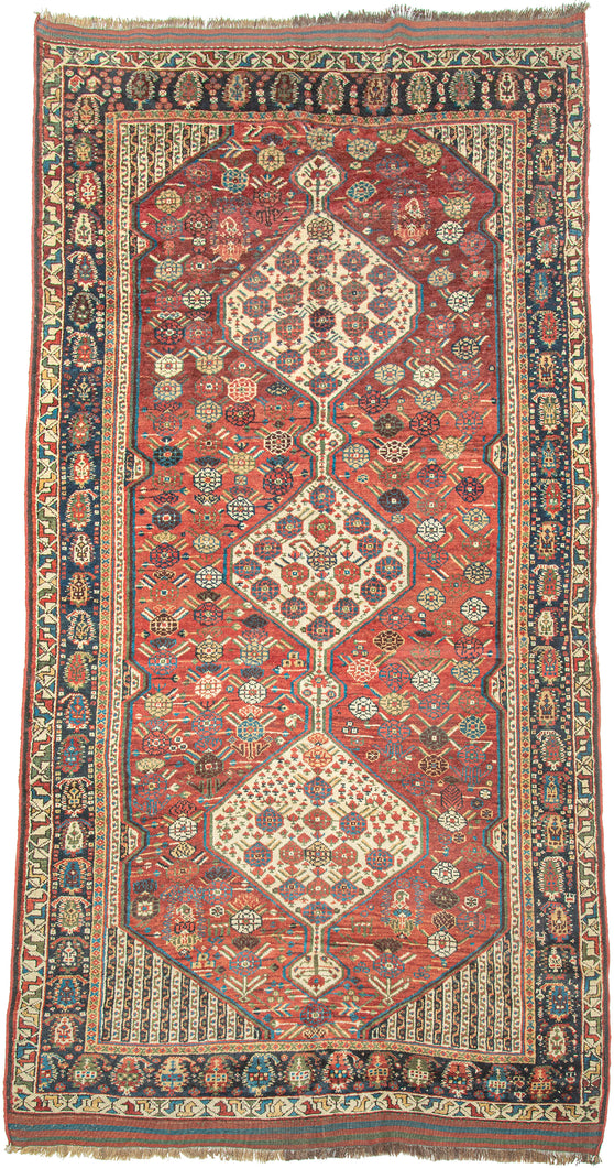 This rug was woven by the Khamseh Confederation during the 19th Century

It features three totemic ivory ground medallions against a rich madder red field and is adorned with a dazzling array of stylized rosettes and abstracted blossoms. It is well balanced by a densely decorated main border of intricate boteh (paisley) motifs. The original blue, green and red striped end kilims are still intact perfectly completing the rug. A good example of this very collectible type.