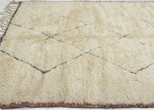 This Beni Ourain rug was woven during the middle of 20th century in the Middle Atlas Mountains of Morocco.

It features a central column of black latticed diamonds on a creamy white ground.&nbsp; Red and brown stripes can be found around the perimeter, most prominently in the striped kilim end borders. Good quality wool in a large format. Often imititated this is the real deal Moroccan shag that Frank Lloyd Wright referred to as "White Giants"&nbsp;