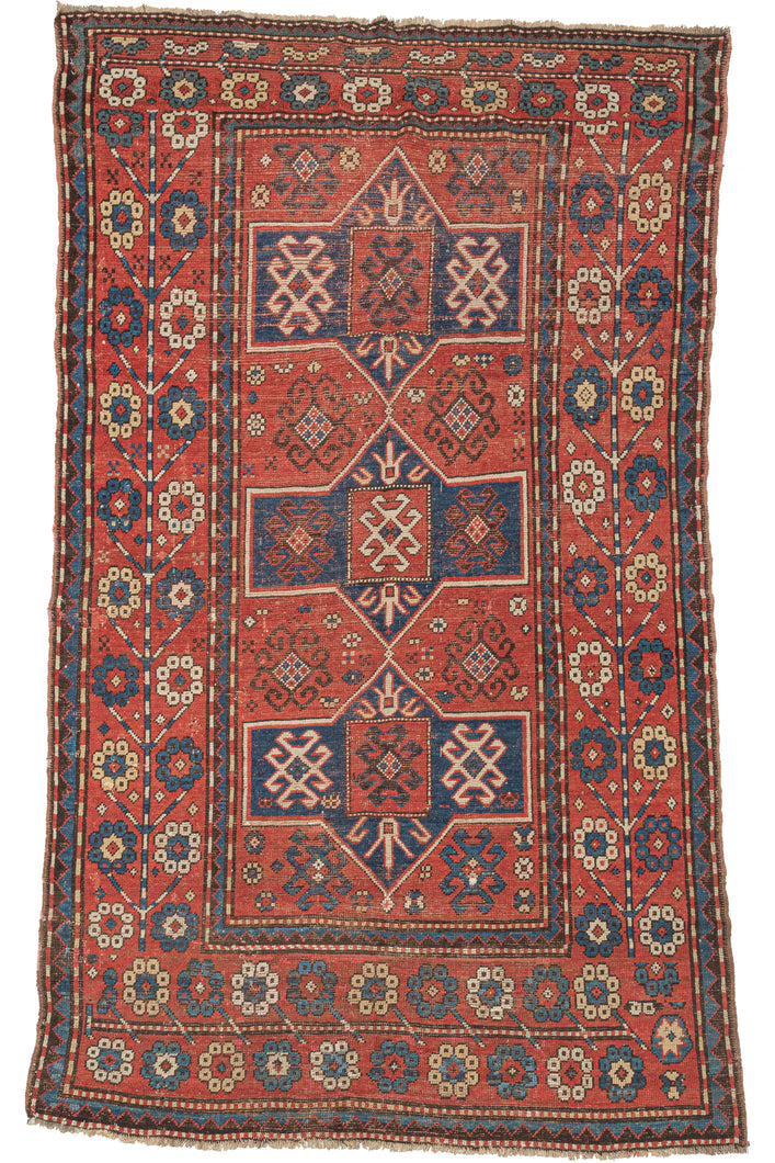 Antique 19th century Kazak rug featuring three navy medallions, on a red ground with a variety of neatly organized protection symbols. But the wide main border composed of large blossoming rosettes on candy cane stems steals the show. In a hard-to-find format for type.