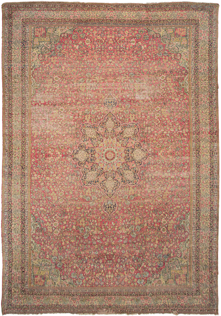 This Lavar Kerman rug was handwoven during latte 19th century in Central Iran.  This oversized rug features a central medallion with a curvilinear floral design and scalloped cornices. The cornices are distinct but have a continuous feel with the central medallion. The field features a vast array of blossoming flowers on patinated fuschia ground.  Tones of yellow, golden wheat, chartreuse, coral and ivory round out the gentle and nuanced palette. 