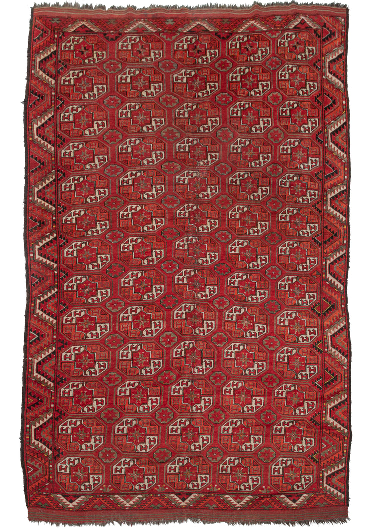 Northern Afghani Turkmen area rug featuring a bold geometric design known as Kizil Ayak. The color palette is made up of bright reds and oranges with black, undyed natural grays and white providing detail and contrast. The whole is framed by a single border.