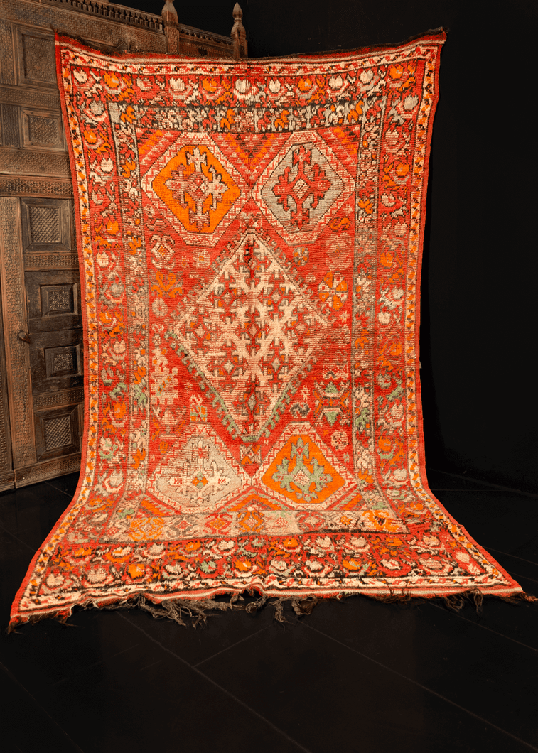 Rabat rug handwoven in Northwest Morocco during middle 20th century. Faded red field with greens, oranges, white and faded black on top. Central asymmetric latched diamond is flanked by four orange sextons and various protection symbols. 