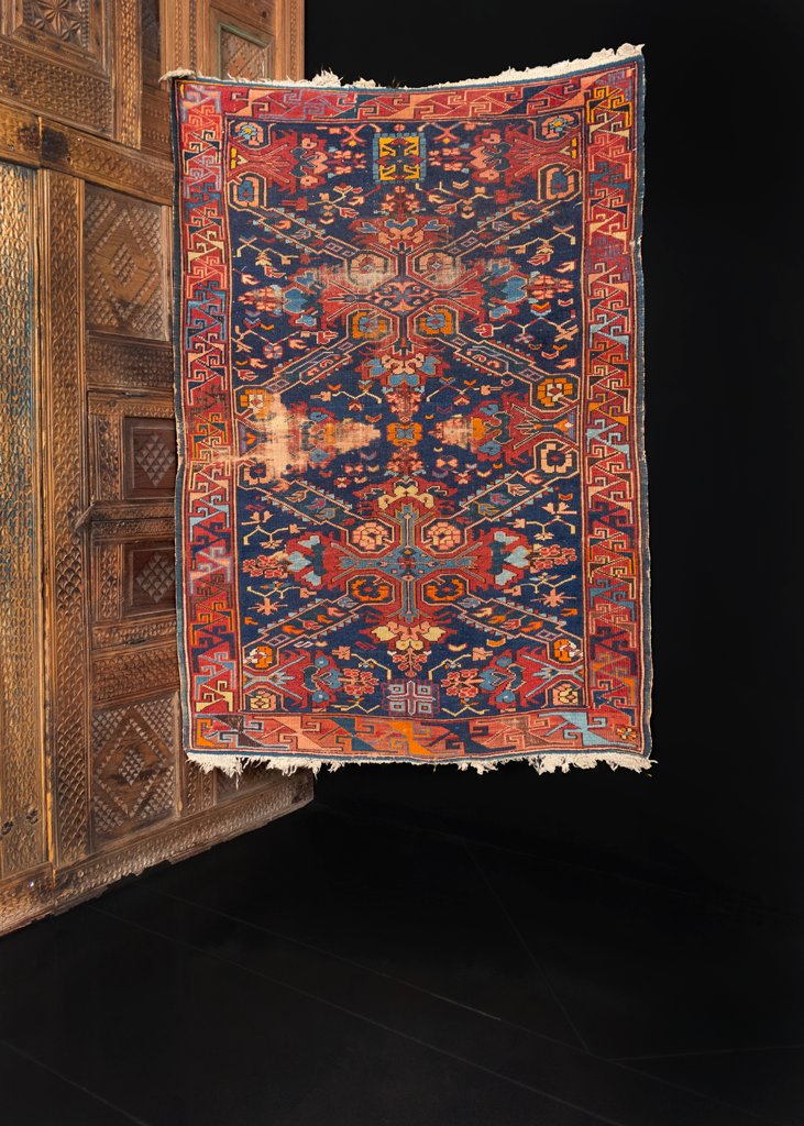 Seychur Kuba rug handwoven early 20th century in the Caucasus. Geometric cross pattern amidst a detailed floral spray. Orange, reds, and pinks atop a dark indigo ground. 