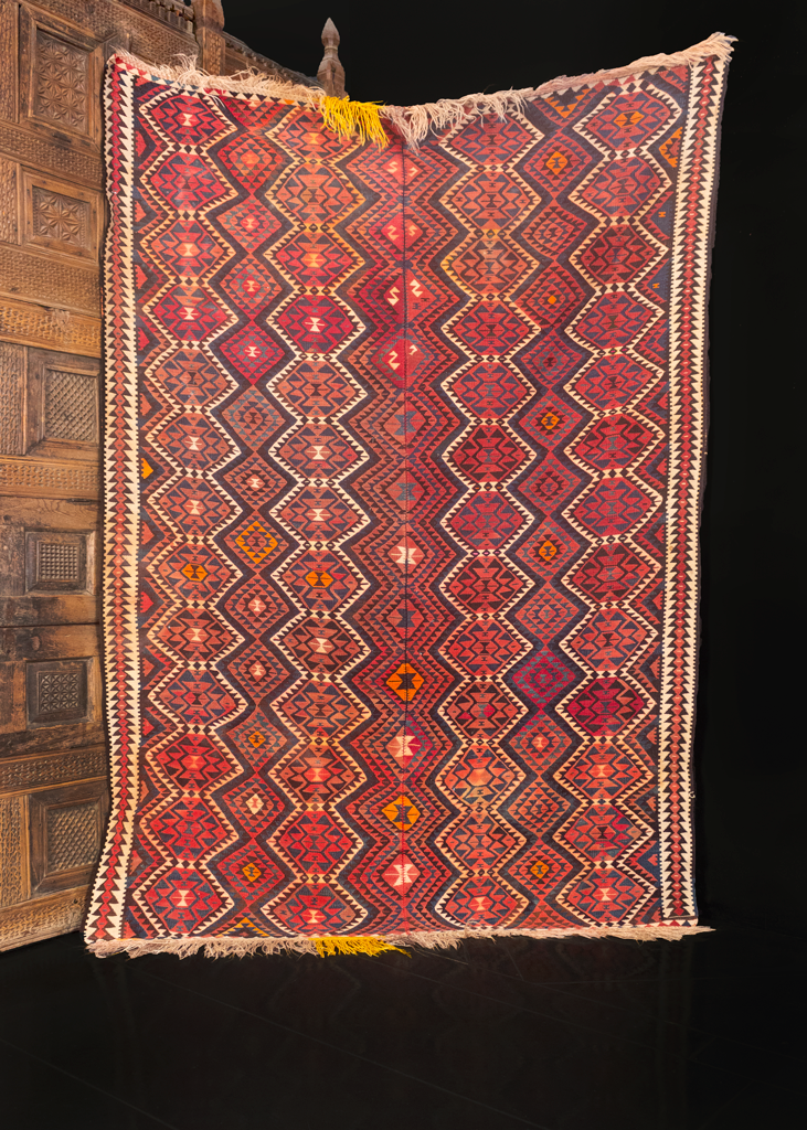 Turkish kilim handwoven during middle of the 20th century. Woven in two panels and stitched down the center. Rows of connected pentagons and diamonds run along the length of the piece. White, orange and yellow atop a red ground. 