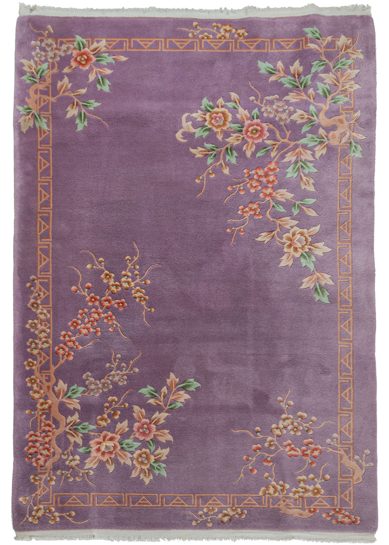 Mid century Chinese deco rug featuring a cheerful purple field. The design is open and borderless, with unique but reciprocating patterning in each corner. Each corner consists of bunches of blossoms in pinks, blues, oranges and greens. The whole is framed by an interlocking 