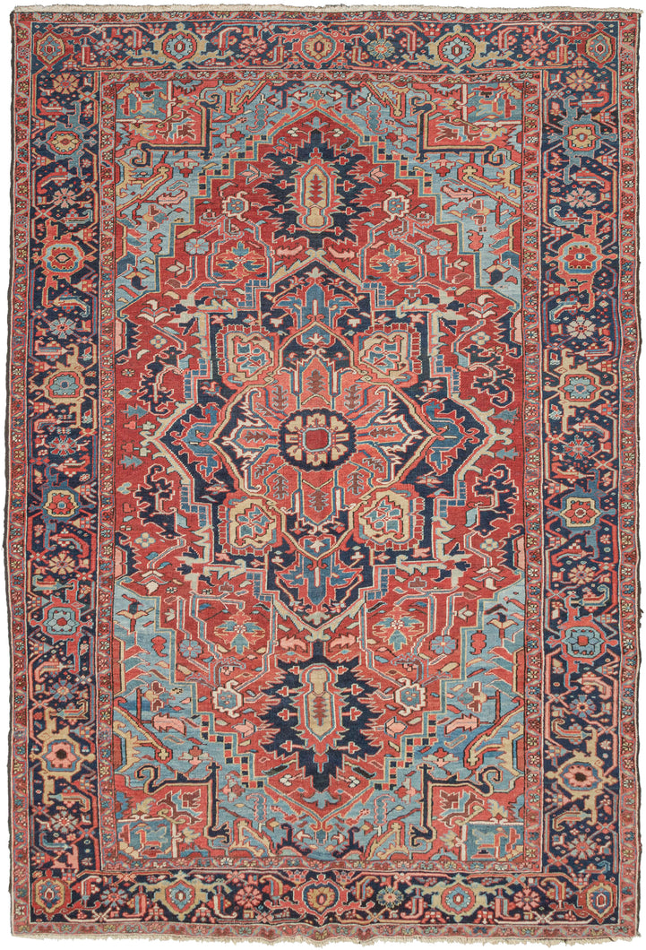 NW Persian Heriz rug featuring a geometric central medallion on rich saturated tones and meaty wool. A brick-red field is complemented by the deep navy, powder blue, yellow, and coral tones with brown and ivory accents. The four powder cornices invigorate the rug and a wonderful undulating abrash adds layers to the composition. It is framed by a main border of alternating palmettes. In a difficult-to-find combo of 7.5' width to 11.5' length.