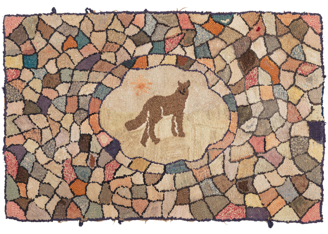 This ANtique Wolf Hooked Rug features a depiction of what appears to be a wolf howling at the sun in its central cartouche. This central is encapsulated by blocks of various colors in an array of shapes pieced together in a lovely mosaic. The fading has made it difficult to differentiate the ground from the sky in the central cartouche. 