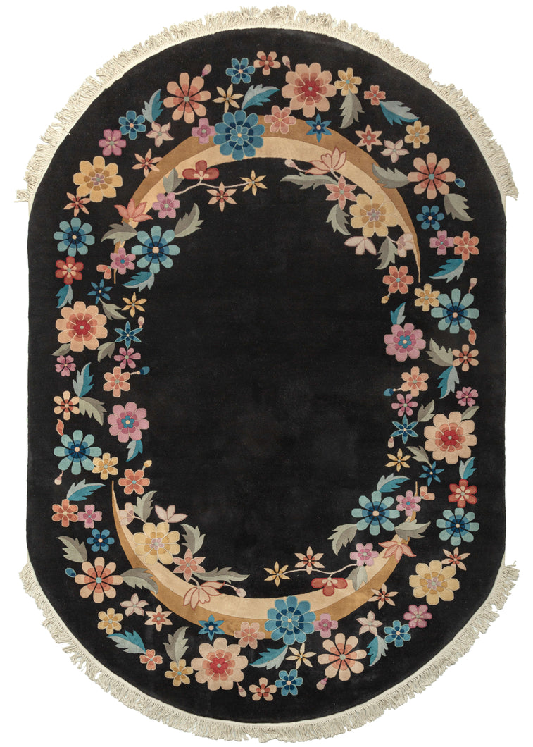 Plush black oval Chinese deco area rug featuring a true black field, with an oval ring of various multicolored flowers. Blue, pink, orange, and yellow blossoms can be identified as stylized peonies, narcissus, chrysanthemum, lotus, plum blossoms, and peach blossoms. The cut-pile technique of cutting piles at different angles to sculpt and shape the wool is used to stunning effect in this rug. 