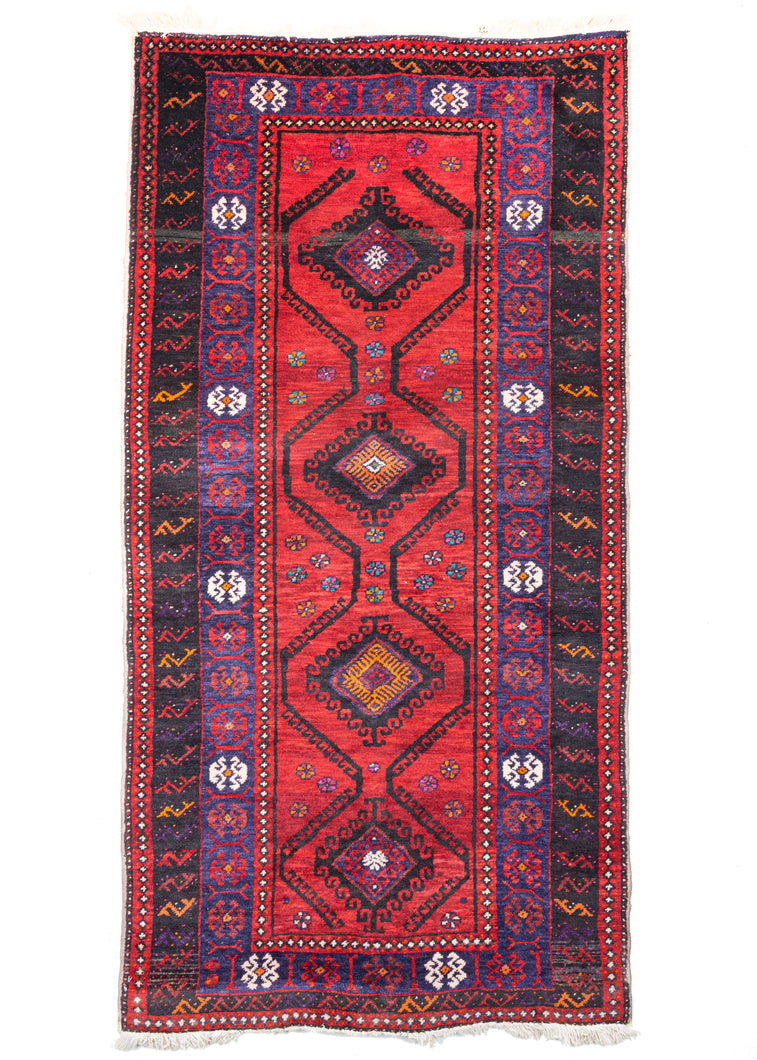 Baluch scatter rug featuring four black latch-hooked medallions surrounded by wavy latch-hooked lines on a vibrant ground with sparse rosettes in lively turquoise, pink, orange and ivory. The ivory is woven utilizing a bright cotton which really pops. There are bright ivory moments in the main border and as well a consistent ivory diamond pattern through the minors borders that kick up the energy level.